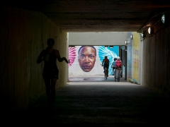 A Mural Featuring the Face of an African American Man Highlighted As A Jogger and Bikers Ride Past.
Image by Michael Bracey